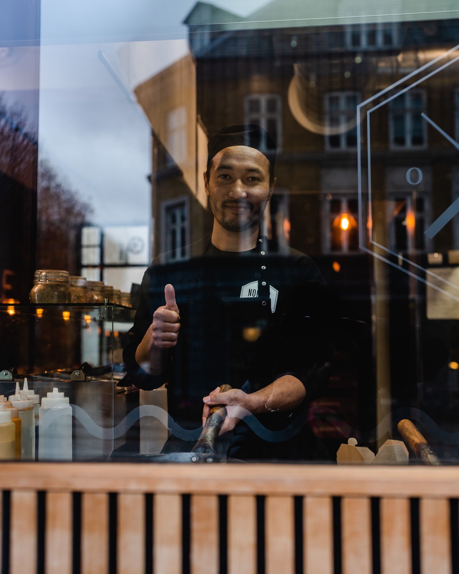 Smilende kok bag vinduet med tommel op